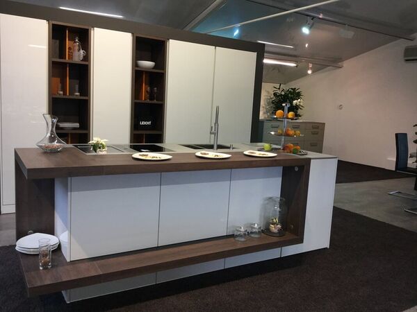 Moderne Einbauküche mit Kochinsel, Holzarbeitsplatte und offenem Regal in Ausstellungsraum.