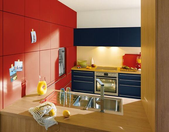 Moderne Küche mit roten und blauen Fronten, Einbauherd und heller Arbeitsplatte.