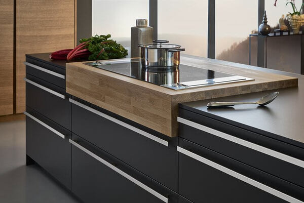 Moderne Küche mit Kochinsel, Induktionskochfeld, Topf, frischen Kräutern und Besteck.